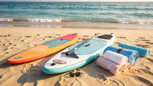 Équipements de natation, planche de paddle et matériel de surf soigneusement disposés sur une plage ensoleillée au bord d’une mer turquoise.