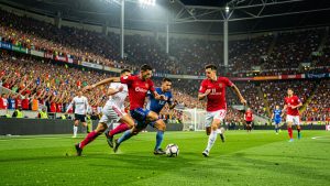 Stade de football international rempli de spectateurs, avec des joueurs en action sur une pelouse éclairée pendant un match de grande compétition.