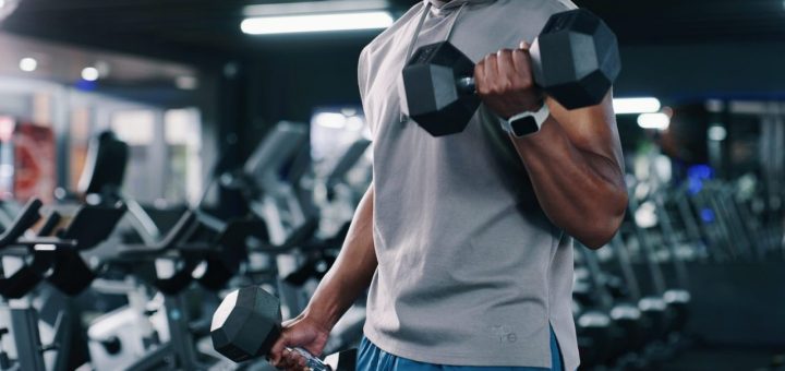 Personne réalisant des exercices avec des haltères de différents poids dans une salle de musculation.