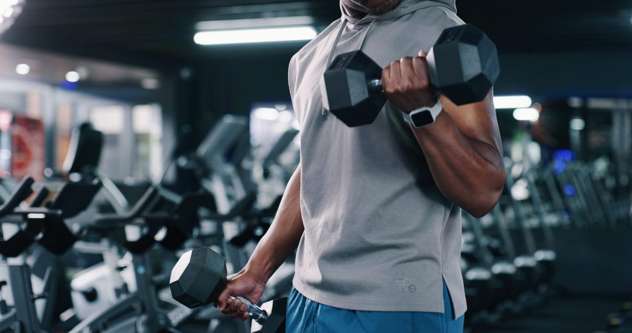 Personne réalisant des exercices avec des haltères de différents poids dans une salle de musculation.